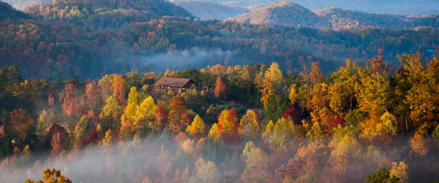 Deck with black rocking chairs, fire pit table, and mountain forest view at sunset