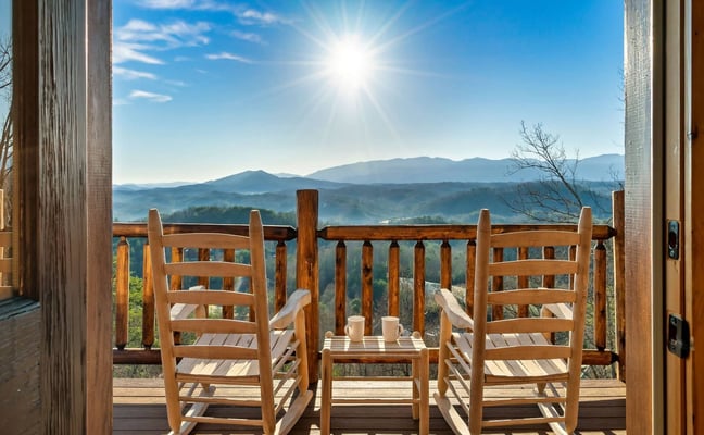 Wooden deck with two rocking chairs overlooking mountain valley under bright sunny sky